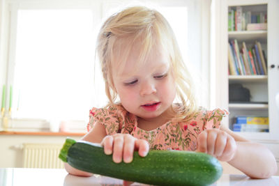 Cute girl holding zucchini at home
