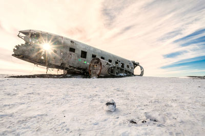 Abandoned airplane crash on snowy field against sky during sunset