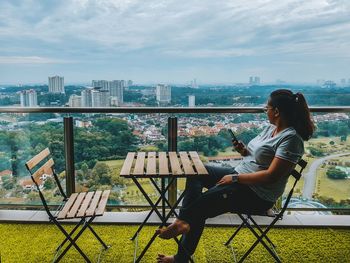 Side view of man sitting on chair against cityscape