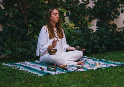 Full length of young woman meditating while sitting outdoors