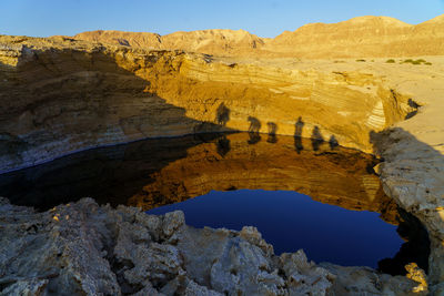 Shadows and reflections of group of people standing by sinkhole on dead sea beach 