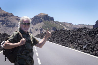 Portrait of man standing on mountain road against clear sky