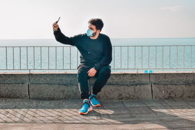 Young man sitting on railing against sea