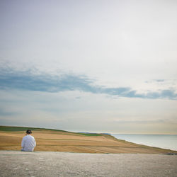 Rear view of boy sitting on cliff against sky