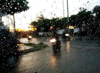 Man riding motorcycle on road seen through wet glass window during rainy season