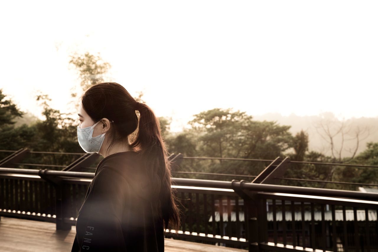 railing, one person, young adult, real people, young women, standing, lifestyles, sky, three quarter length, architecture, women, leisure activity, nature, connection, adult, hair, long hair, hairstyle, side view, outdoors, bridge - man made structure, beautiful woman