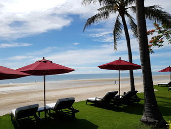 Lounge chairs and palm trees on beach against sky