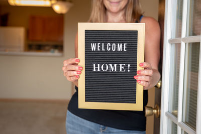 Midsection of woman holding sign at home