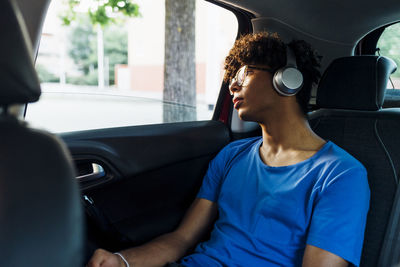 Young man listening music through wireless headphones looking out of car window