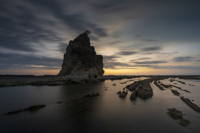 Rock formation in sea against sky during sunset