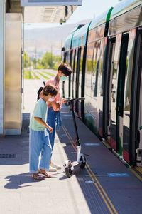 Full length of mother and daughter wearing mask standing on railroad station platform