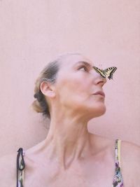 Butterfly on nose of mature woman against wall