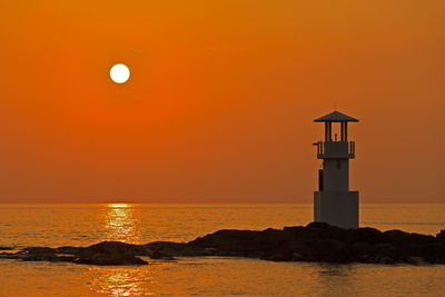 Silhouette lighthouse by sea against sky during sunset