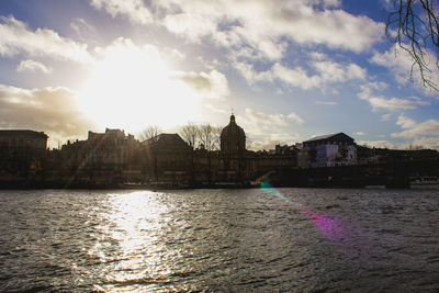 View of buildings by river against cloudy sky