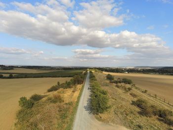 Empty road amidst field against sky