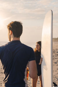 Male and female surfers with surfboard at beach during sunset