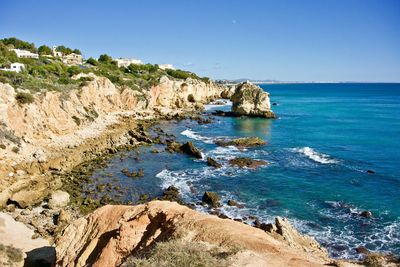 Rock formations by sea against clear blue sky