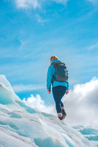 Rear view of woman walking on snow against blue sky