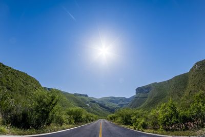 Road amidst trees against clear blue sky