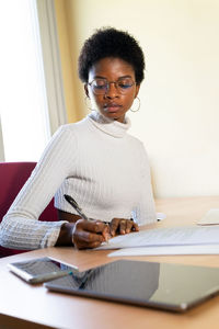 Black female physician writing information on paper sheet while preparing medical report at table in office of modern clinic