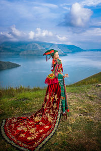 Woman wearing traditional clothing while standing on mountain against lake
