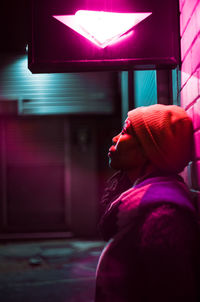 Side view of woman standing by wall at night