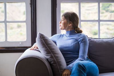 Side view of young woman using laptop while sitting on sofa at home