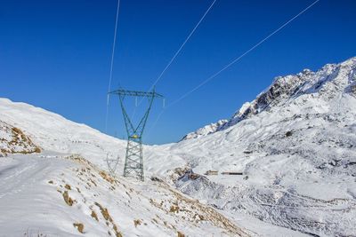 Power line on snow covered mountain against blue sky