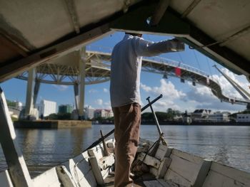 Rear view of man standing on boat in river