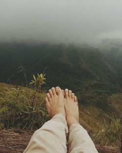 Low section of woman relaxing on mountain during foggy weather