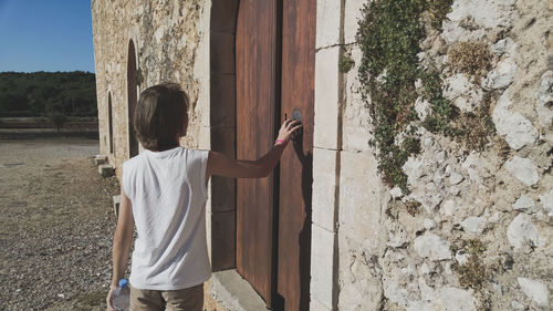 Rear view of teenage boy knocking door while standing outdoors