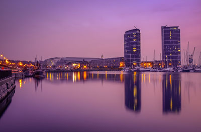 Scenic view of lake by illuminated buildings at dusk