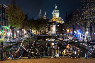 Bicycles on street by illuminated buildings in city at night