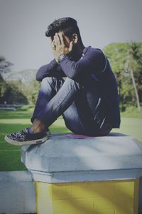 Side view of young man sitting on retaining wall