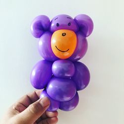 Close-up of hand holding balloon teddy bear against white background