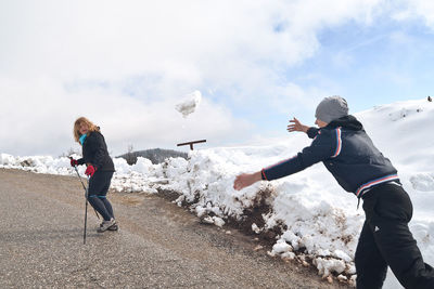 Man throwing snow at woman with hiking pole while climbing mountain during winter