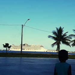 Rear view of man looking at swimming pool against clear blue sky