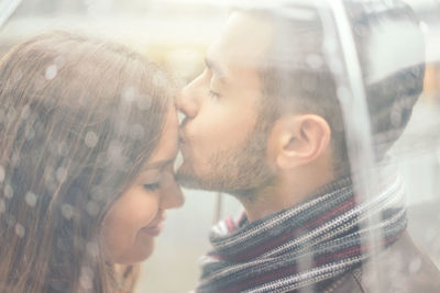 Close-up of man kissing on woman forehead seen through umbrella