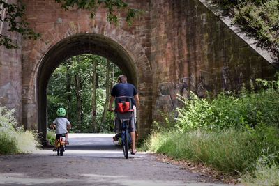 Rear view of father and son riding bicycle on road