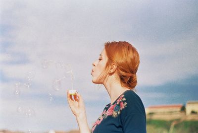 Close-up of a young, red headed woman blowing bubbles