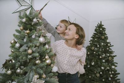 Smiling mother giving daughter piggyback ride to put star on christmas tree