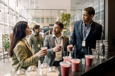 Male and female business professionals discussing while holding drink glasses during break at convention center