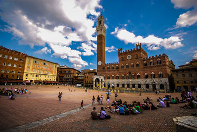 Group of people in town square against cloudy sky