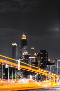 Illuminated light trails on road by buildings against sky at night