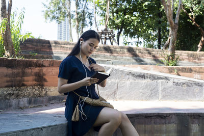 Young woman using mobile phone while sitting on tree