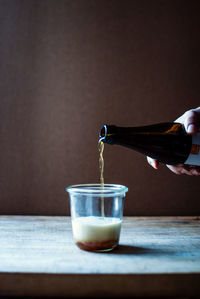 Cropped hand of woman pouring beer in glass on table