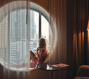 Side view of woman sitting on window sill at home