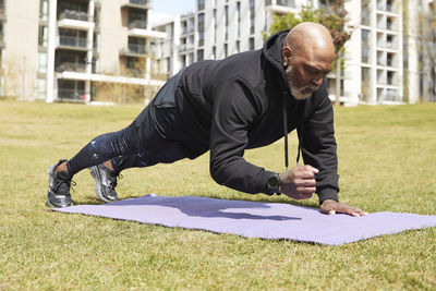 Man practicing plank position on exercise mat in public park