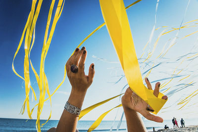 Cropped hands of woman with kites at beach against sky