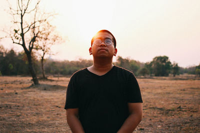 Portrait of young man standing on field against sky